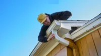 Installateur ajustant un coude de descente blanche sous un ciel bleu