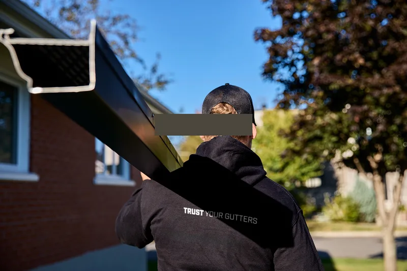 Technicien transportant une section de gouttière noire sur l'épaule